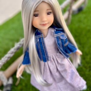 May include: A doll with long, silver hair and brown eyes, wearing a lavender dress and a blue denim jacket. The doll is posed outdoors on a green surface, with a rope in the background.