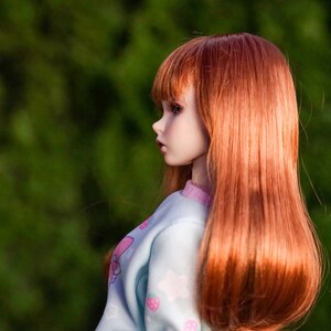 May include: A doll with long, straight, auburn hair wearing a light blue and pink sweater with a strawberry print.