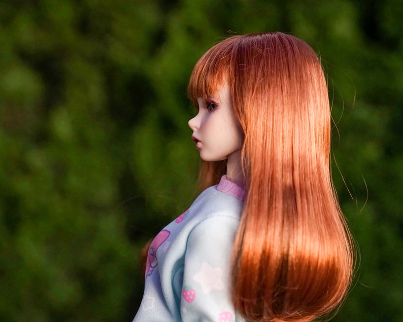 May include: A doll with long, straight, auburn hair wearing a light blue and pink sweater with a strawberry print.