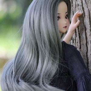 May include: A doll with long, silver-grey hair, wearing a black dress. The doll is looking to the side and has a slight smile on her face.
