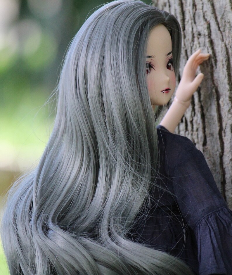 May include: A doll with long, silver-grey hair, wearing a black dress. The doll is looking to the side and has a slight smile on her face.