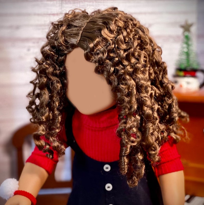 May include: A doll with long, curly brown hair wearing a red turtleneck sweater and a black overall dress with white buttons.