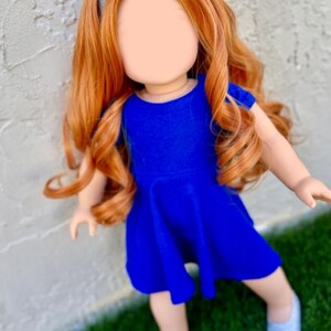 May include: A doll with long, curly, auburn hair wearing a blue dress and a silver headband. The doll is standing on green grass.