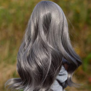 May include: A doll with long, wavy, silver-grey hair. The doll is wearing a light grey sweater.