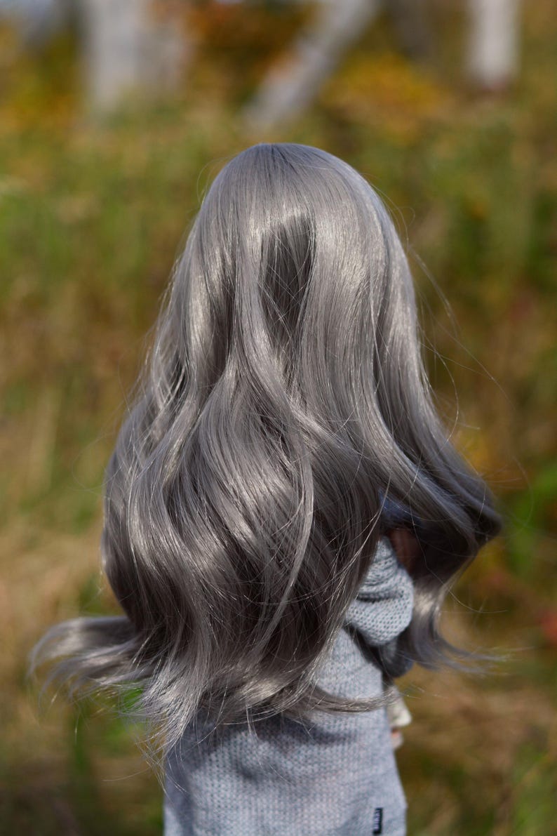 May include: A doll with long, wavy, silver-grey hair. The doll is wearing a light grey sweater.