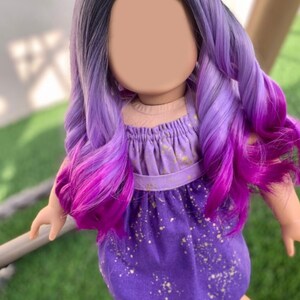 May include: A doll with long, wavy, two-toned purple and magenta hair. The doll wears a purple dress with gold speckles and a matching halter top. The doll is standing on green grass.