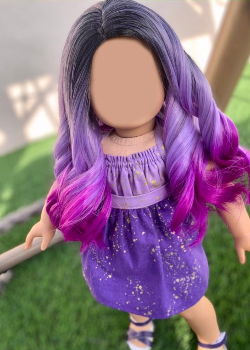 May include: A doll with long, wavy, two-toned purple and magenta hair. The doll wears a purple dress with gold speckles and a matching halter top. The doll is standing on green grass.