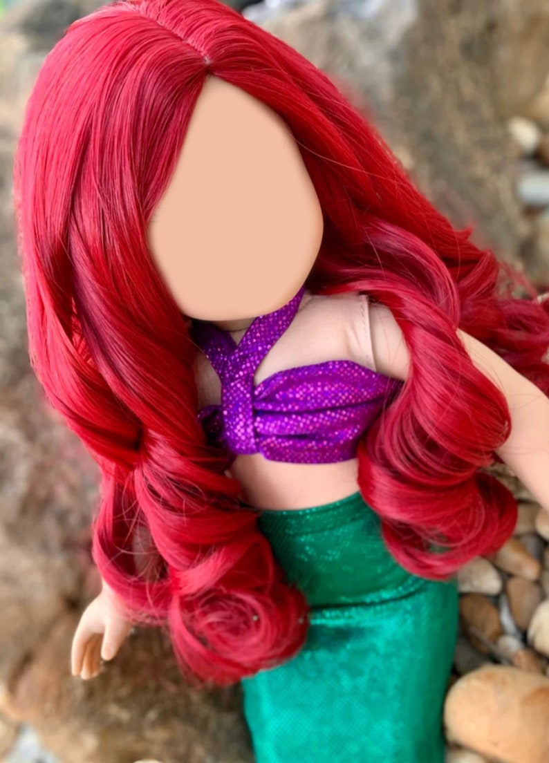 Puede incluir: Una peluca roja con el pelo largo y rizado, dise&ntilde;ada para una mu&ntilde;eca. La mu&ntilde;eca lleva un disfraz de sirena morado y verde.