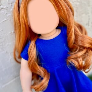 May include: A doll with long, curly, auburn hair wearing a blue dress and a silver headband.