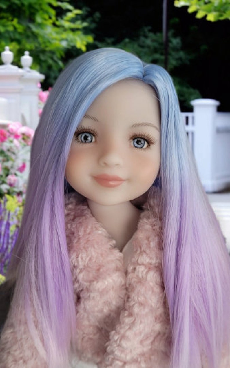 May include: A doll with long, straight, ombre hair that transitions from light blue to lavender. The doll is wearing a pink fuzzy jacket.
