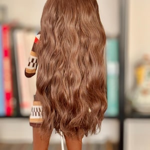May include: A long, wavy brown wig with a natural-looking texture. The wig is styled in a loose, flowing style, with the ends of the hair falling just below the shoulders.