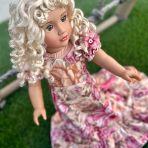 May include: A doll with blonde curly hair wearing a pink and brown floral dress. The doll is looking to the right of the image.