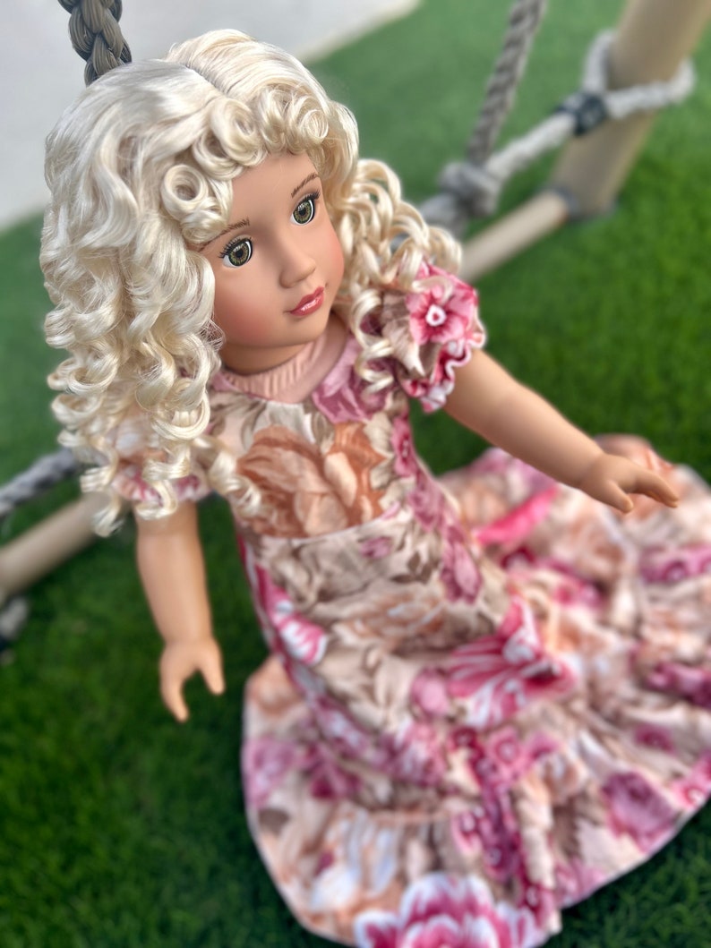 May include: A doll with blonde curly hair wearing a pink and brown floral dress. The doll is looking to the right of the image.