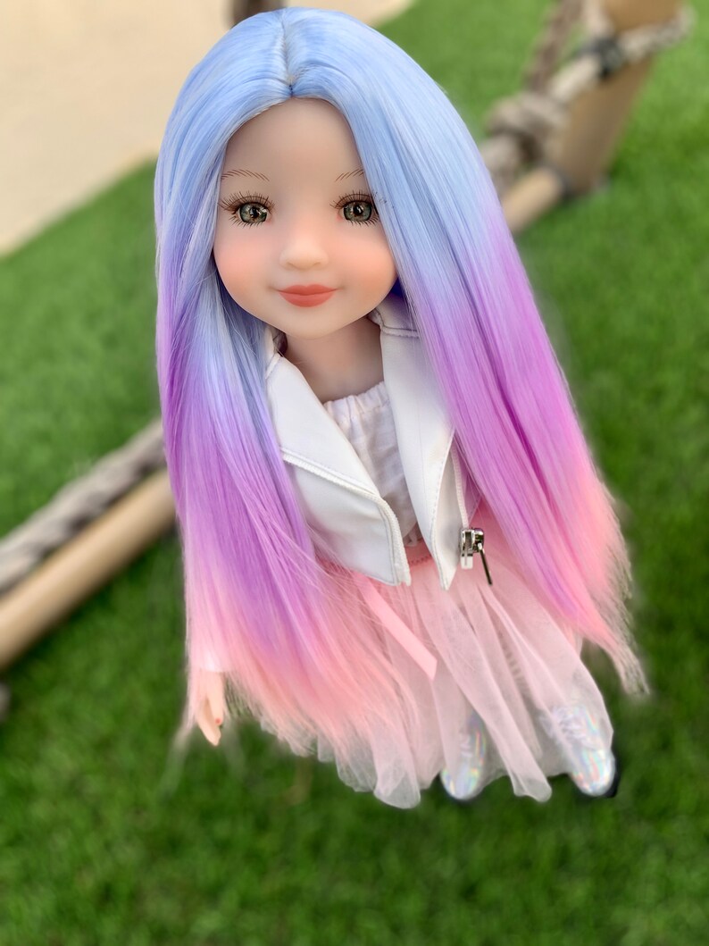 May include: A doll with long, ombre hair that transitions from light blue to purple to pink. The doll is wearing a white jacket, a pink tulle skirt, and sparkly shoes.