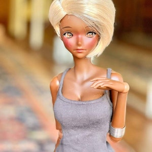 May include: A doll with dark skin and blonde hair wearing a gray tank top and black pants.