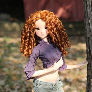 May include: A doll with long, curly, auburn hair wearing a purple, cropped, button-up shirt and blue jeans.