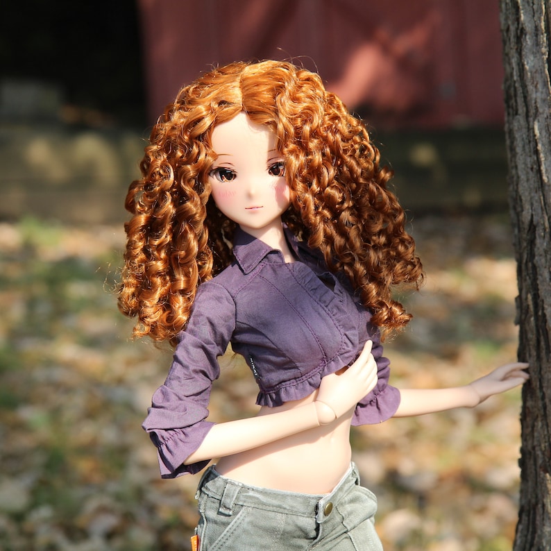 May include: A doll with long, curly, auburn hair wearing a purple, cropped, button-up shirt and blue jeans.