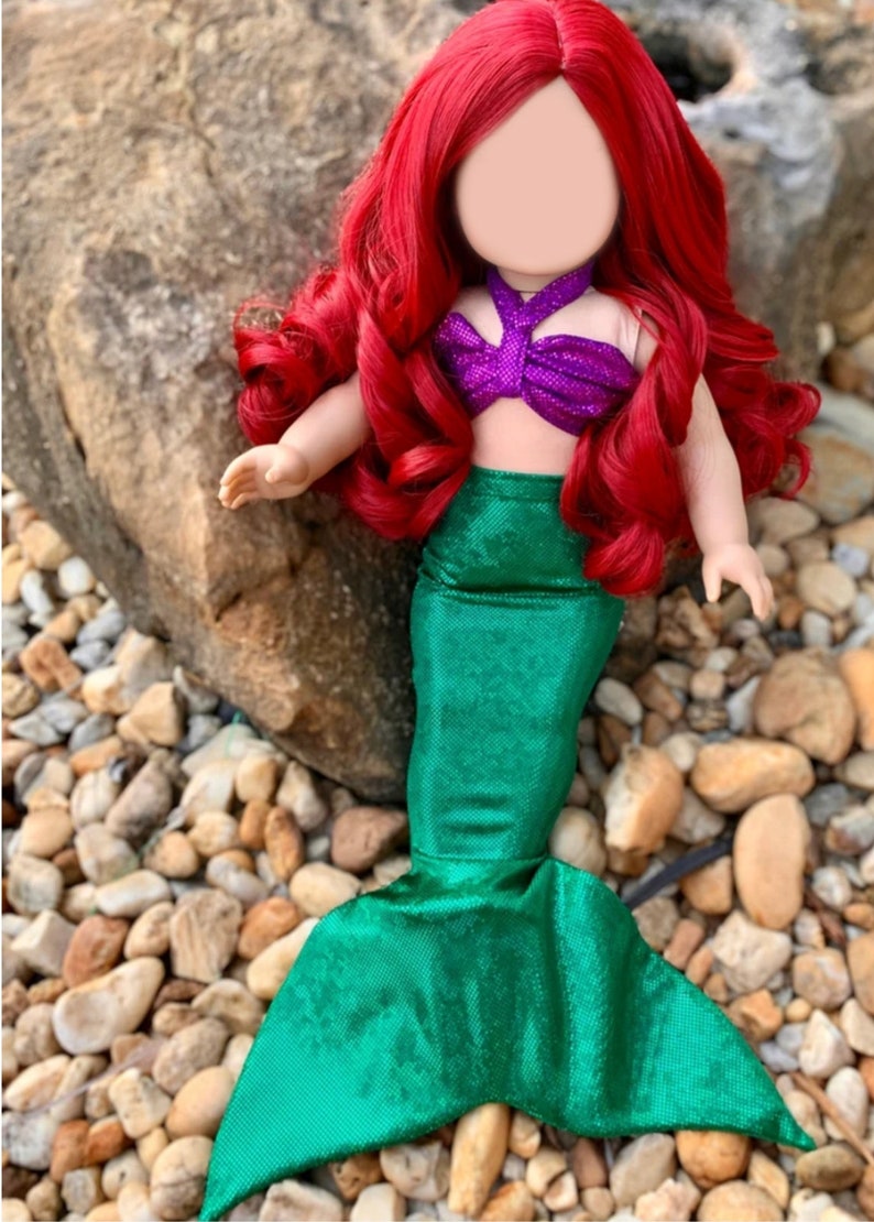 Puede incluir: Una mu&ntilde;eca de pelo rojo con un disfraz de sirena morado y verde. La mu&ntilde;eca tiene una cola verde con un acabado brillante.