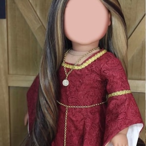 May include: A doll wearing a red dress with gold trim and a gold chain belt. The doll has long brown and blonde hair and is wearing a gold necklace with a sparkly pendant.