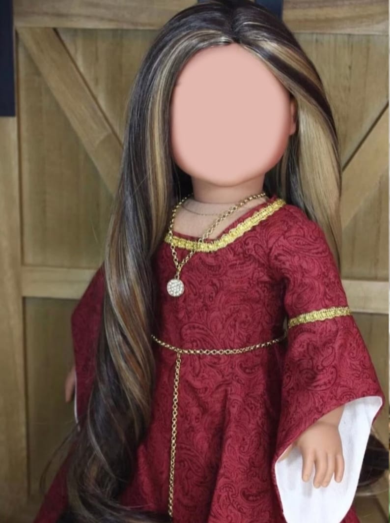May include: A doll wearing a red dress with gold trim and a gold chain belt. The doll has long brown and blonde hair and is wearing a gold necklace with a sparkly pendant.