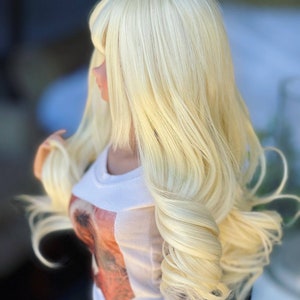 May include: A long, wavy, blonde wig with bangs. The wig is styled in loose curls and has a natural-looking finish.