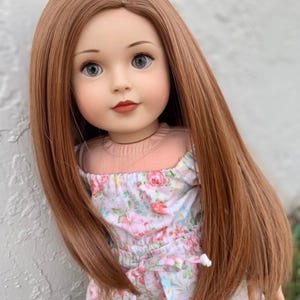 Può includere: Una bambola con capelli lunghi, lisci e castano rossicci, che indossa un vestito a stampa floreale.