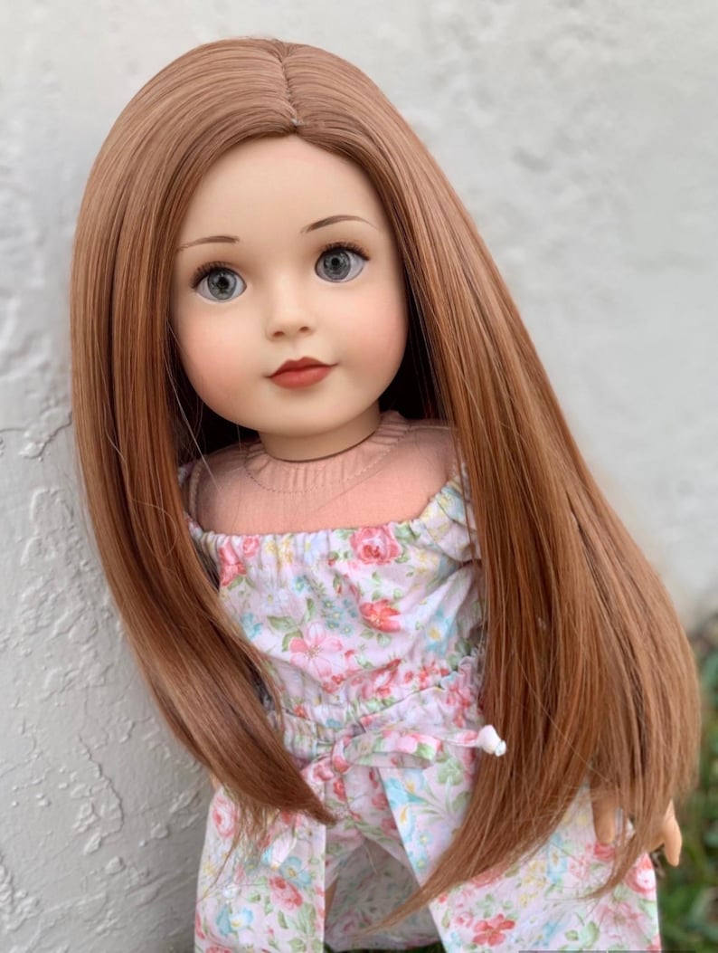 May include: A doll with long, straight, auburn hair wearing a floral print dress.