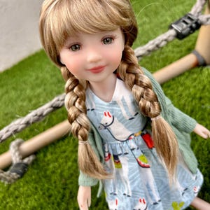 May include: A doll with long blonde hair in braids wearing a light blue dress with a llama print and a light green cardigan.