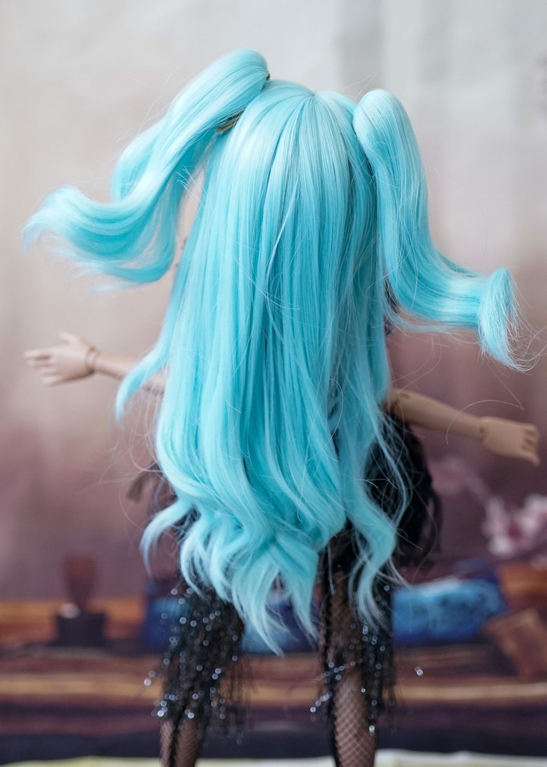 Puede incluir: Una mu&ntilde;eca con el pelo largo y azul brillante peinado en dos coletas altas. El pelo es ondulado y fluido. La mu&ntilde;eca lleva un vestido negro con lentejuelas.