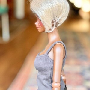 May include: A doll with a short, platinum blonde wig. The doll is wearing a gray tank top and black pants.