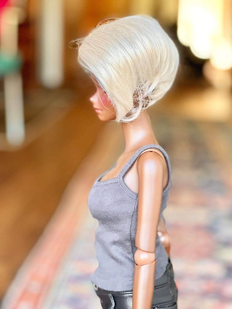 May include: A doll with a short, platinum blonde wig. The doll is wearing a gray tank top and black pants.