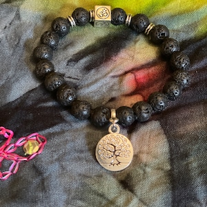 May include: Black lava rock beaded bracelet with a silver Om charm and a silver tree of life charm.