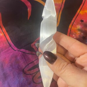 May include: A white selenite crystal wand with a spiral design. The wand is smooth and polished, with a pointed tip.