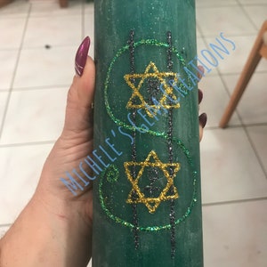 May include: A green candle with gold glitter and two gold six-pointed stars with a black outline. The candle has the text "MICHELE'S CREATIONS" written on it.