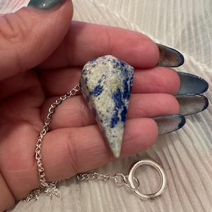 May include: A white and blue crystal pendulum with a silver chain and ring. The crystal is a pointed shape and has a speckled pattern.