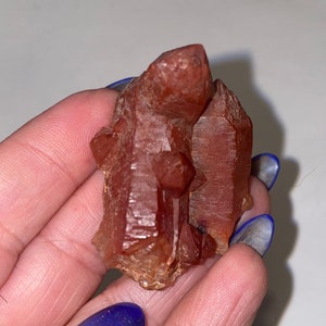 May include: A cluster of red quartz crystals with a pointed shape. The crystals are translucent and have a reddish-brown color.