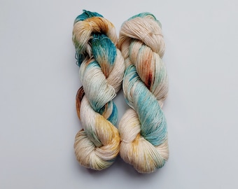 May include: Two skeins of yarn in a cream, brown, and teal colourway. The yarn is hand-dyed and has a variegated colour pattern.