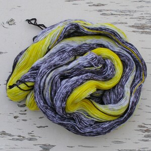 May include: A skein of yarn in a black and yellow colourway. The yarn is hand-dyed and has a variegated pattern.