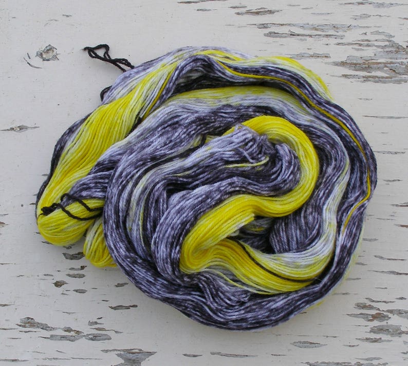 May include: A skein of yarn in a black and yellow colourway. The yarn is hand-dyed and has a variegated pattern.