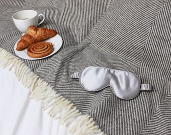 May include: A gray and white striped blanket with a silver sleep mask and a plate with two pastries and a cup of coffee.