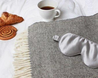 May include: A gray silk sleep mask on a gray and white blanket with a croissant and a cinnamon roll on a white plate.