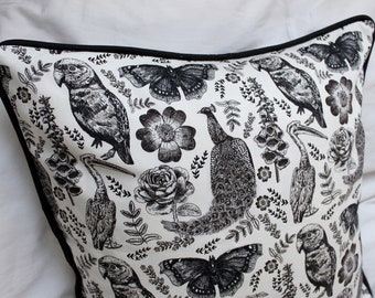 May include: Black and white throw pillow with a repeating pattern of birds, butterflies, and flowers. The pillow has a black border.