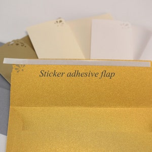 K&ouml;nnte beinhalten: Ein Satz Umschl&auml;ge in verschiedenen Farben, darunter Gold, Elfenbein und Grau. Der goldene Umschlag hat einen Klebeverschluss und ein dekoratives Ausschnittmuster.