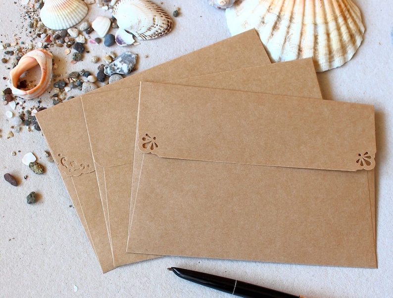 Puede incluir: Un conjunto de cuatro sobres de papel kraft marr&oacute;n con dise&ntilde;os decorativos recortados en la solapa superior.