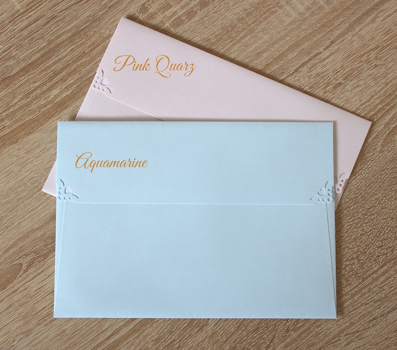 May include: Two envelopes, one light blue and one light pink, with decorative cutouts and the words "Aquamarine" and "Pink Quartz" printed in gold.