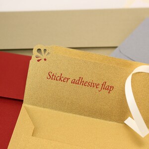 May include: A gold envelope with a red sticker adhesive flap. The envelope has a decorative cut-out design on the top edge. The envelope is open and the flap is folded back.