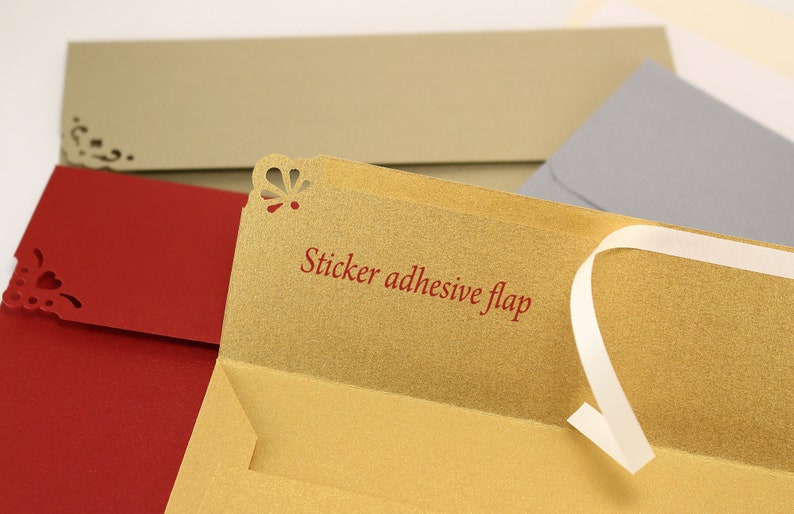May include: A gold envelope with a red sticker adhesive flap. The envelope has a decorative cut-out design on the top edge. The envelope is open and the flap is folded back.