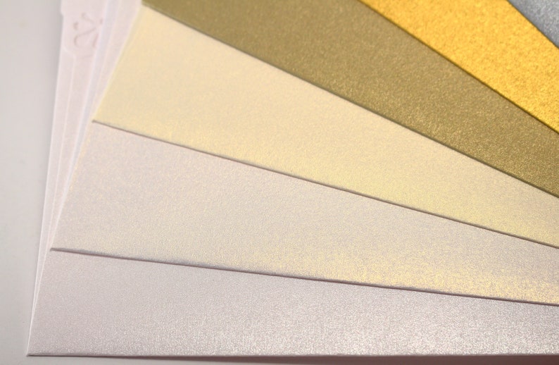 May include: A fan of different colored paper with a subtle shimmer. The colors are white, cream, light yellow, gold, and green.