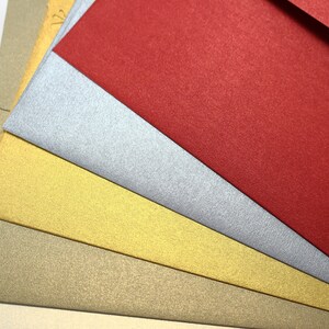 May include: Five different colored envelopes, stacked on top of each other. The top envelope is red, followed by silver, gold, beige, and ivory.