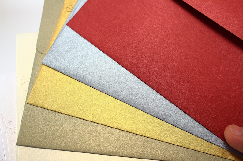 May include: Five different colored envelopes, stacked on top of each other. The top envelope is red, followed by silver, gold, beige, and ivory.
